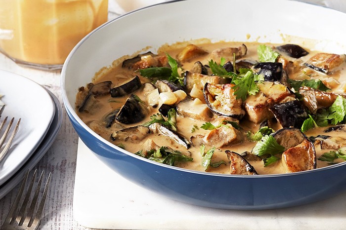 Bowl of creamy aubergine curry with a plate of forks and rice at the side