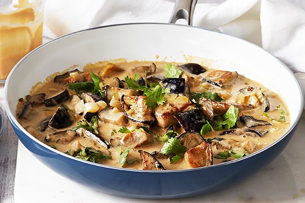 Bowl of creamy aubergine curry with a plate of forks at the side