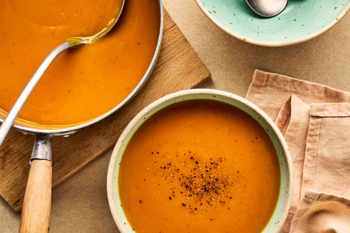 A pan and bowl of sweet potato soup next to an empty bowl with spoons