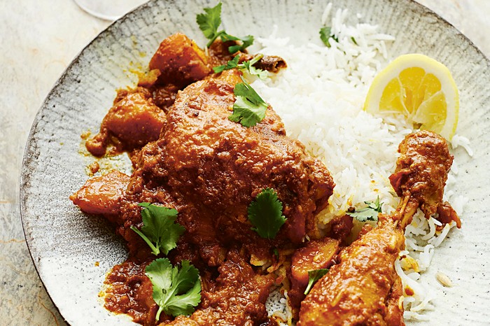 A plate topped with chicken thigh curry with white rice on the side