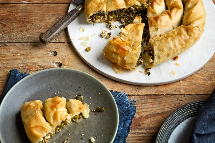 A circular filo pastry tart filled with green kale and feta, with a slice taken out of it and put on a side plate