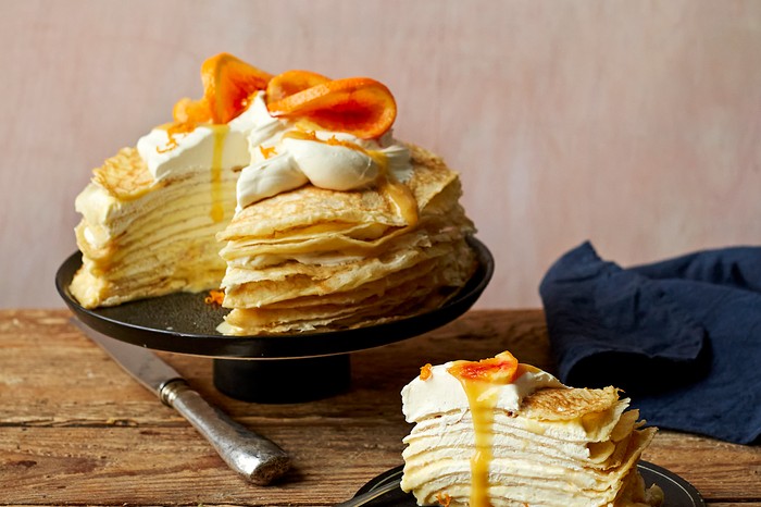 A black cake stand topped with a crepe cake, whipped cream and blood orange slices