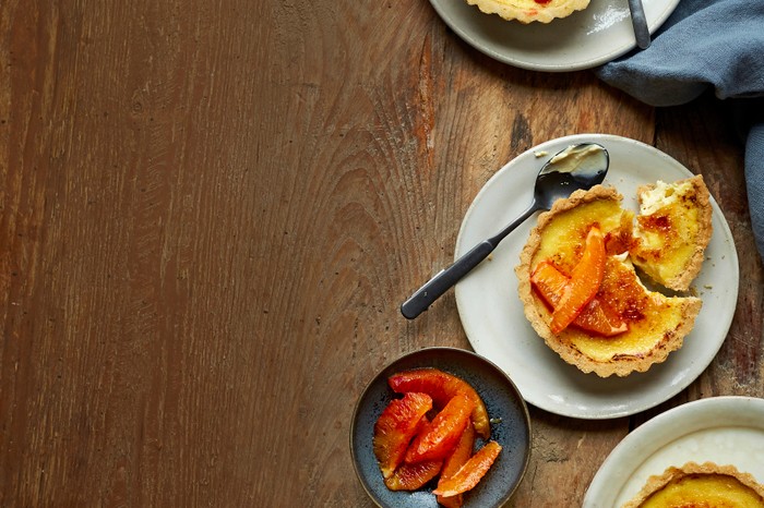 Three white plates topped with small pastry tarts filled with custard and slices of blood orange