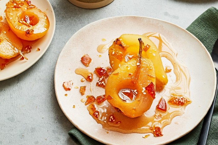 plated filled with poached pear with a pot of custard and green linen napkin