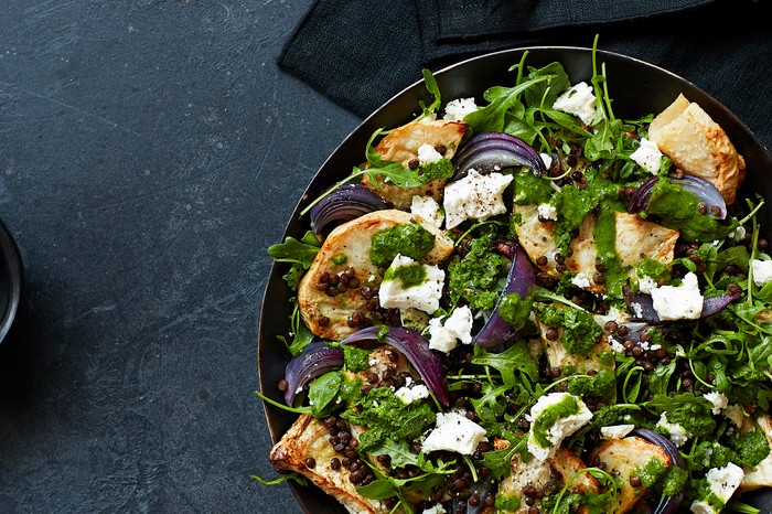 A black bowl filled with a green chopped salad with feta and croutons