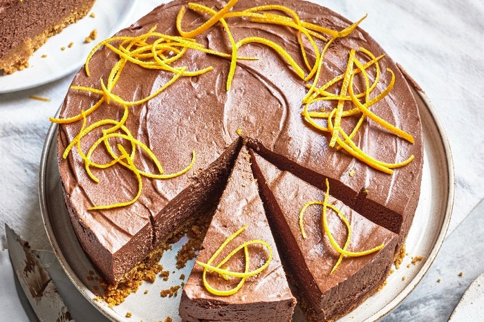 A chocolate cheesecake on a white plate with strips of orange zest on top