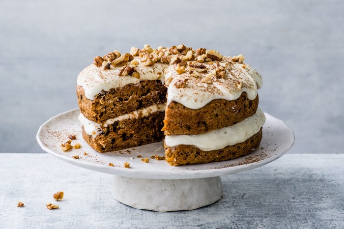 Vegan carrot cake topped with walnuts on a white cake stand