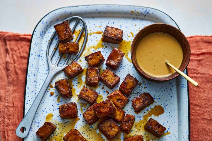 A baking try of crispy baked tofu with a dressing on the side