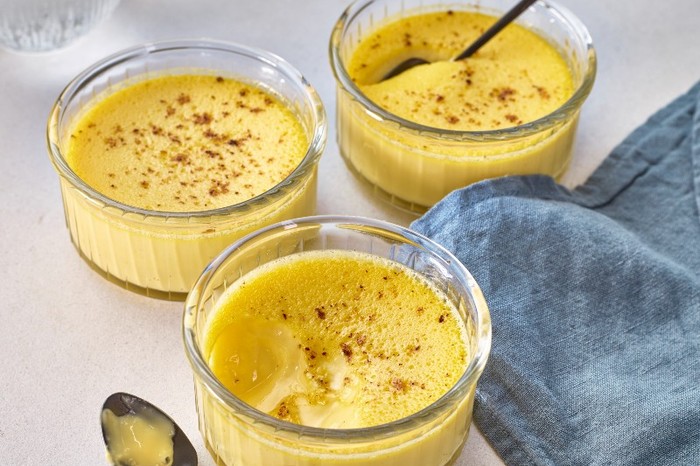 Three glass ramekins of custard with silver spoons on a blue napkin