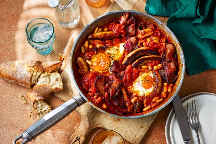 a full english breakfast in metal pan sat on a wooden chopping board