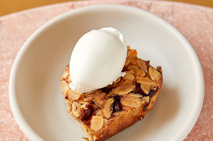 A white bowl filled with an almond sponge, flecked with flaked almonds and topped with a quenelle of mascarpone