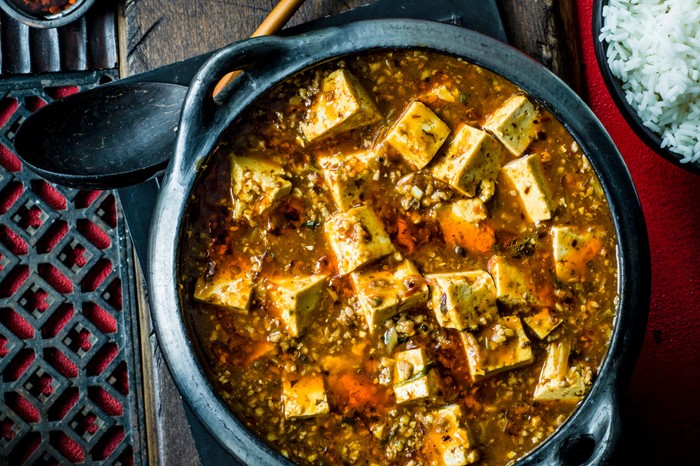 Large pan of mapo tofu next to a bowl of rice