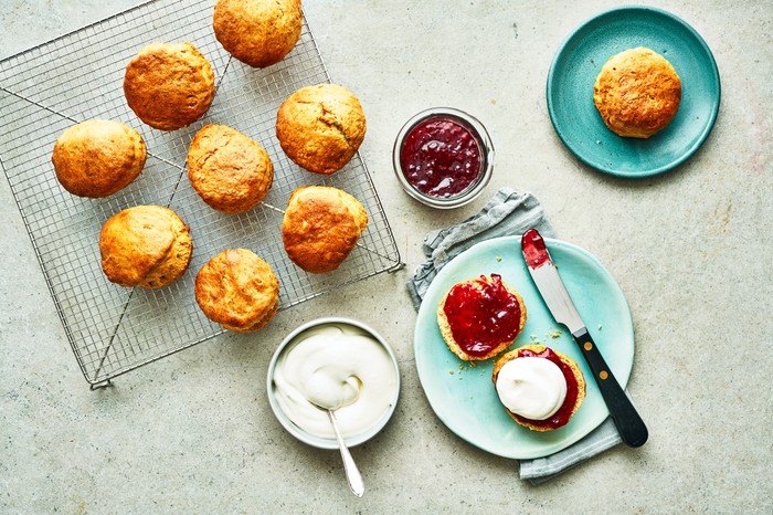 A batch of golden vegan scones on a cooling rack, with a pot of cream and jam