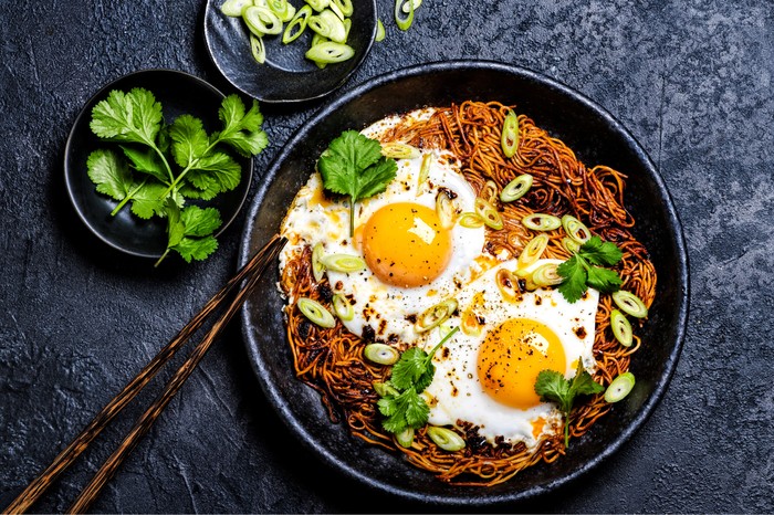 Crispy instant ramen noodles in a skillet with two fried eggs on top and coriander leaves