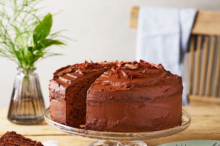 A chocolate cake on a glass cake stand with a slice taken out of it