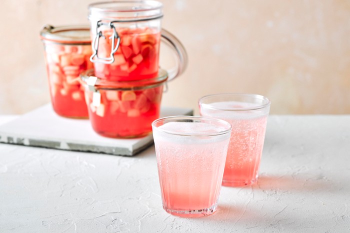 Rhubarb gin and tonic in a glass with a jar of rhubarb behind