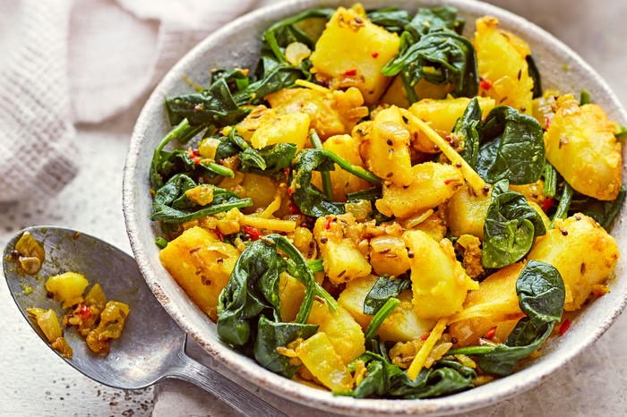 Bowl of saag aloo next to a spoon