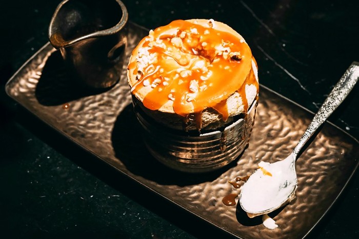 A salted caramel popcorn soufflé in a ramekin on a plate with a small pot of sauce