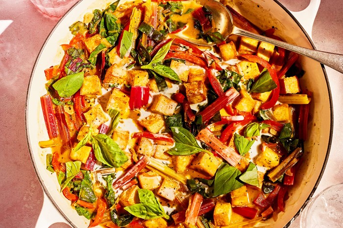 A large white pan of tofu and swiss chard curry with a serving spoon