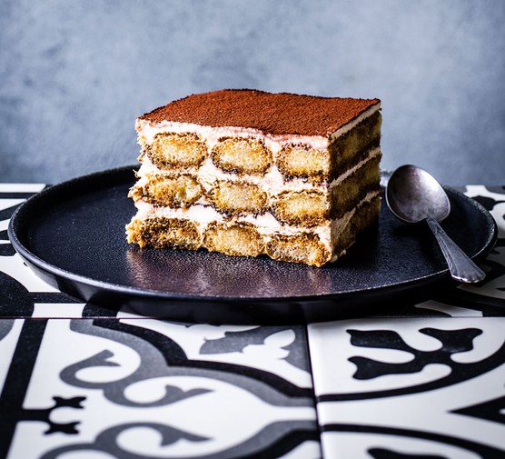 A large slice of tiramisu on a dark plate