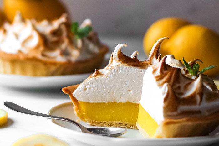 A lemon meringue pie on a white plate with a large slice cut out of it