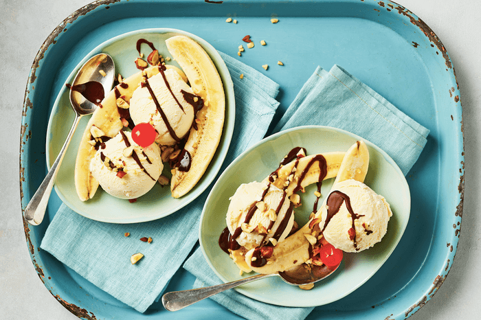 A blue enamel tray holding two blue plates of banana split, drizzled in chocolate sauce