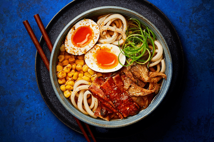 Brunch udon in a bowl with boiled eggs, bacon, sweetcorn and mushrooms